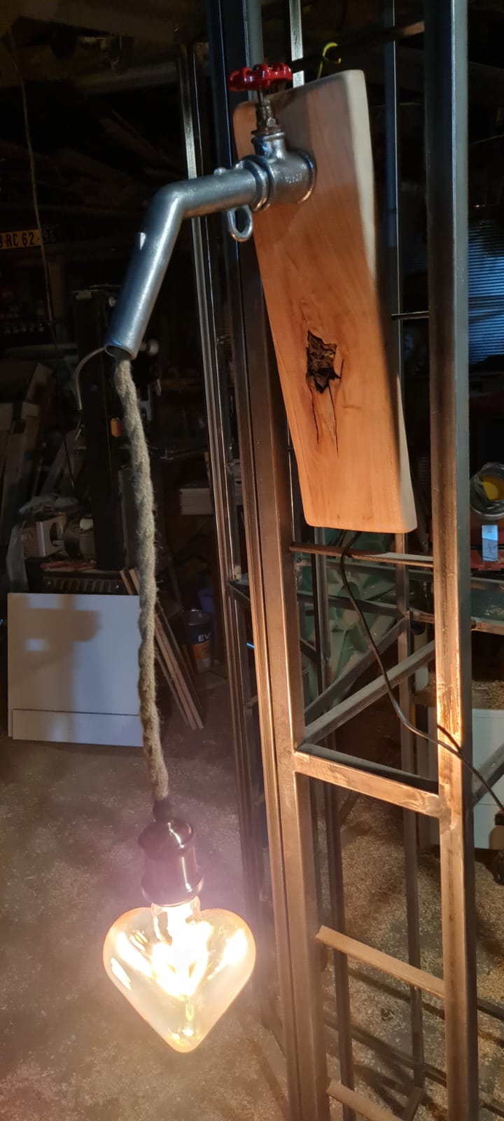 Applique lumineuse : robinet et corde laissant couler une ampoule en forme de cœur sur une planche de bois
